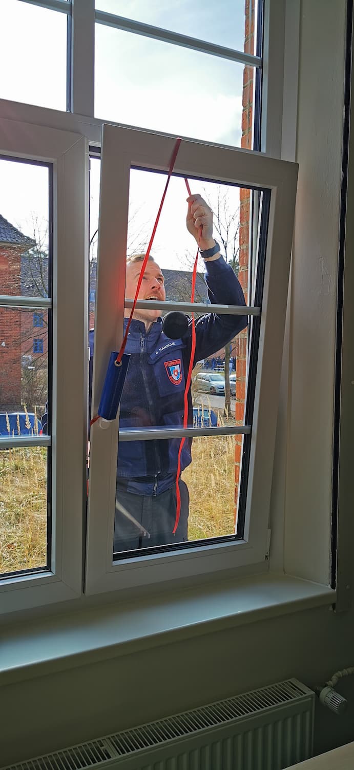 Ein Feuerwehr Anwärter versucht ein Fenster von außerhalb zu öffnen.